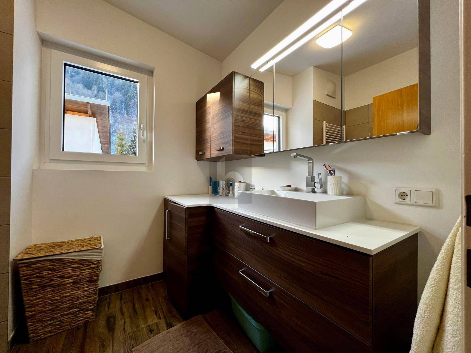 Modernes Badezimmer mit dunklem Holzwaschtisch, integriertem Waschbecken und großem Spiegelschrank.