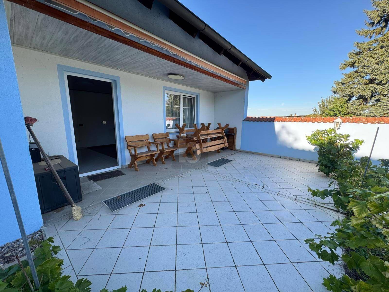 Geflieste Terrasse mit Holzbänken und Zugang zum Haus, ideal für Entspannung im Freien.
