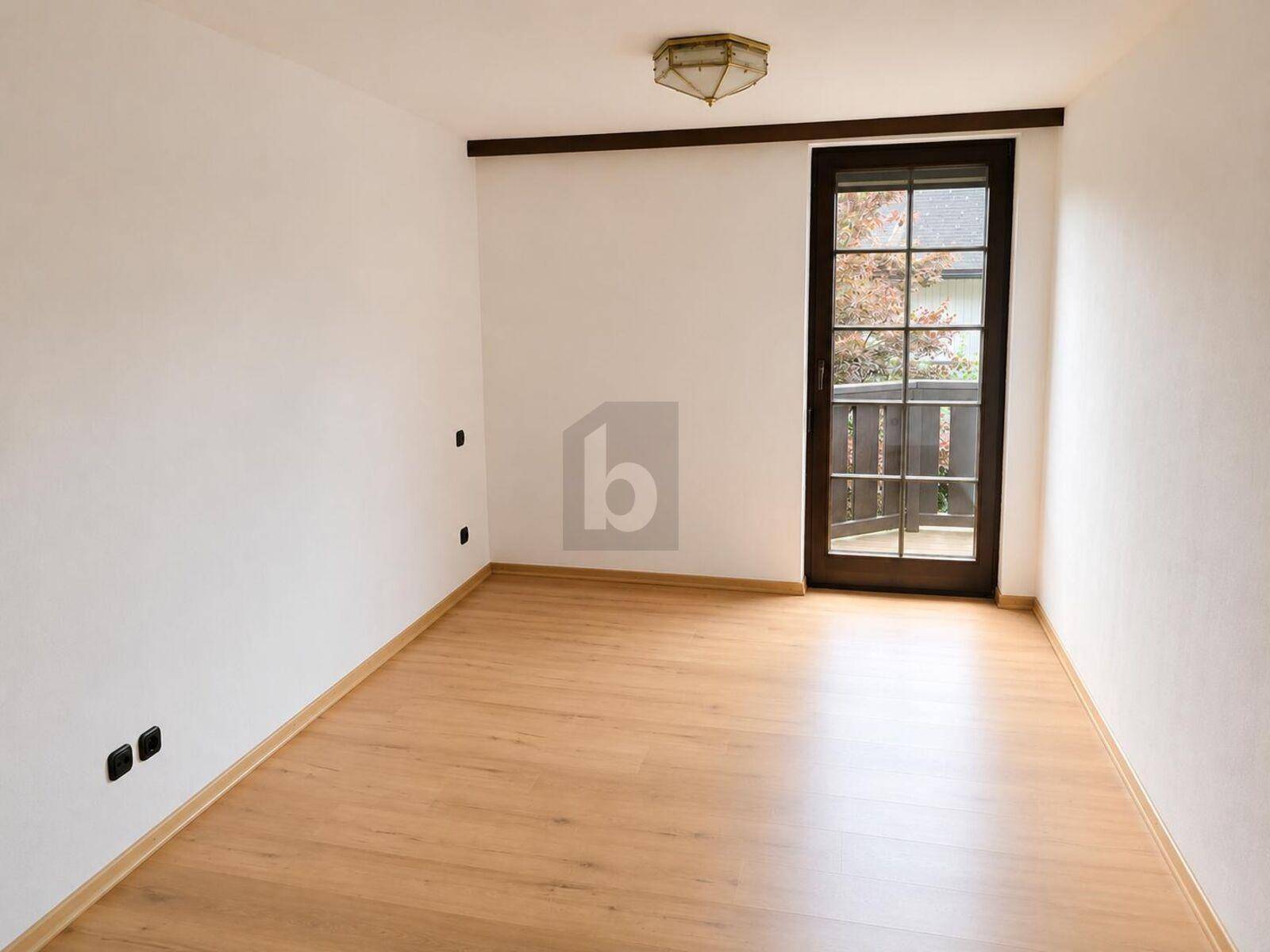 Helles, leeres Zimmer mit Laminatboden und direktem Zugang zu einem kleinen Außenbereich.