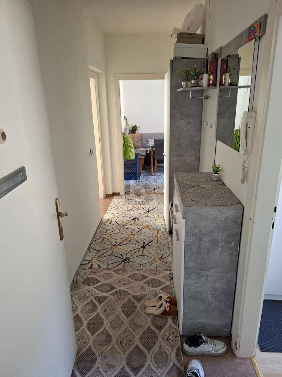 Schmaler Flur mit Spiegel, Schuhschrank und Teppichläufer.