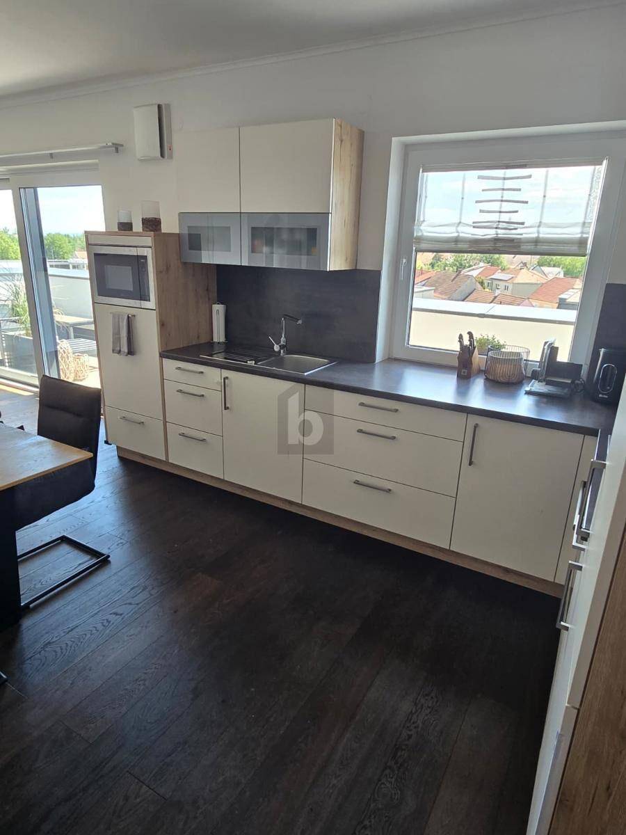 Moderne Einbauküche mit hellen Fronten, Holzakzenten und einem Fenster mit Blick nach draußen.