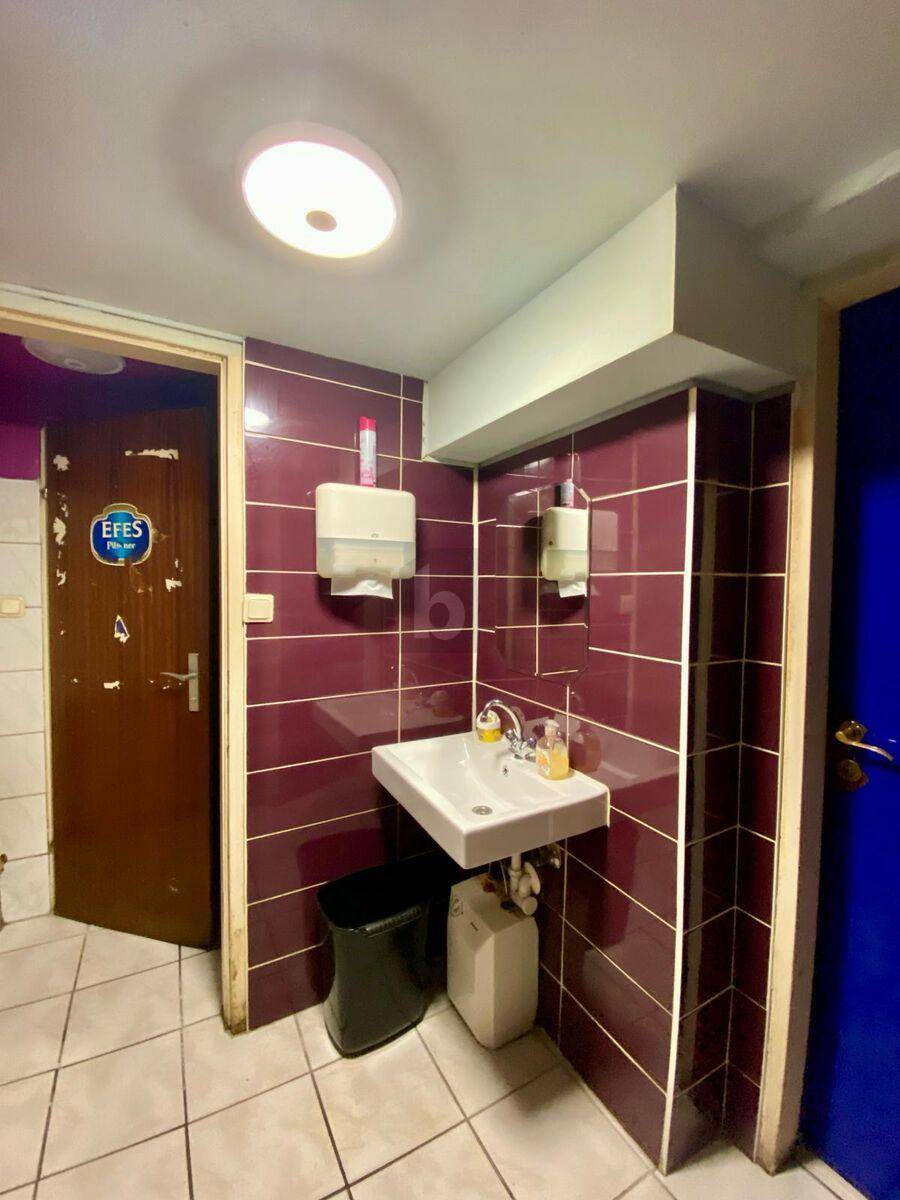 Kleines Badezimmer mit Waschbecken, Spiegel, Papierhandtuchspender und dunkelroten Wandfliesen.