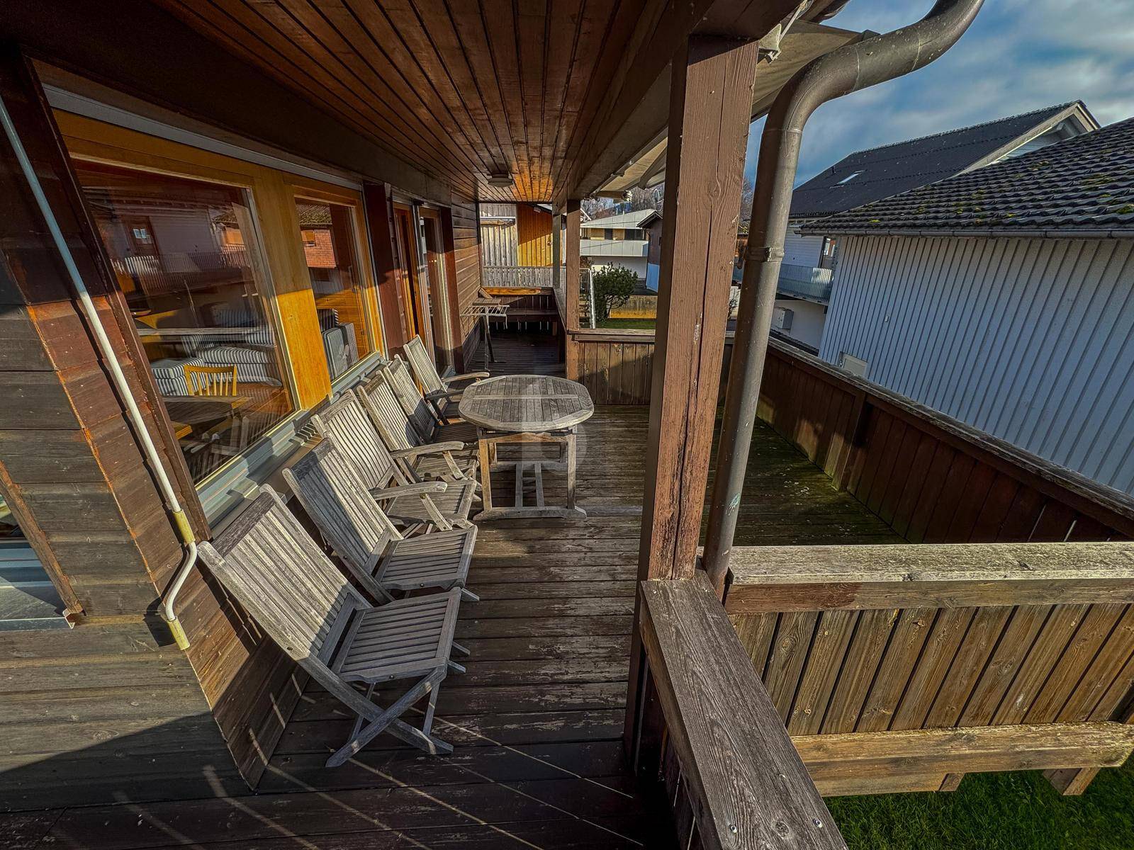 Gemütliche Holzterrasse mit Sitzgelegenheiten und Blick auf die Nachbarschaft an einem sonnigen Tag.