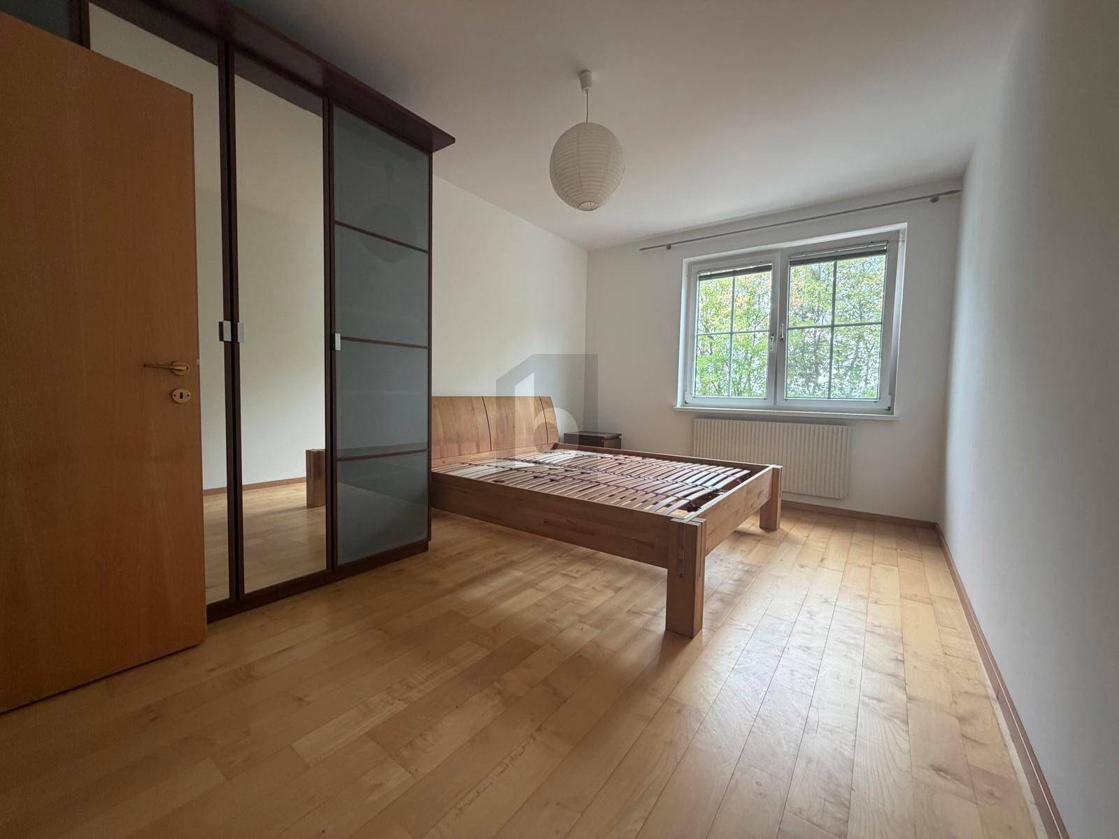 Schlafzimmer mit Holzbettrahmen, großem Spiegelschrank und Parkettboden, bietet viel Stauraum.