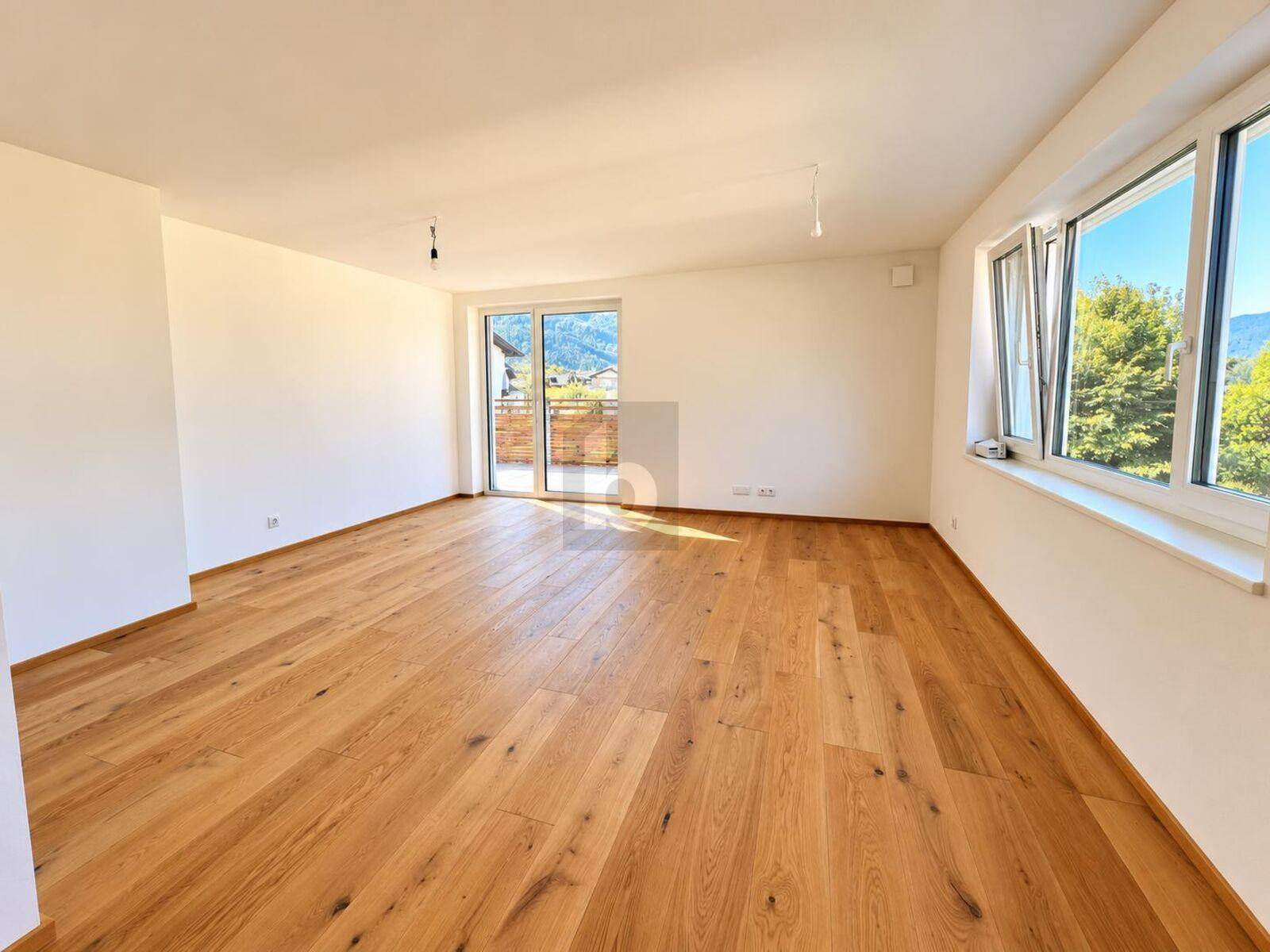 Lichtdurchfluteter Raum mit Holzboden und mehreren Fenstern mit Blick ins Grüne.