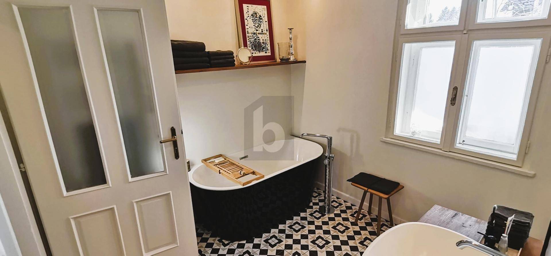 Modernes Badezimmer mit freistehender schwarzer Badewanne, Fenster und gemusterten Fliesenboden.