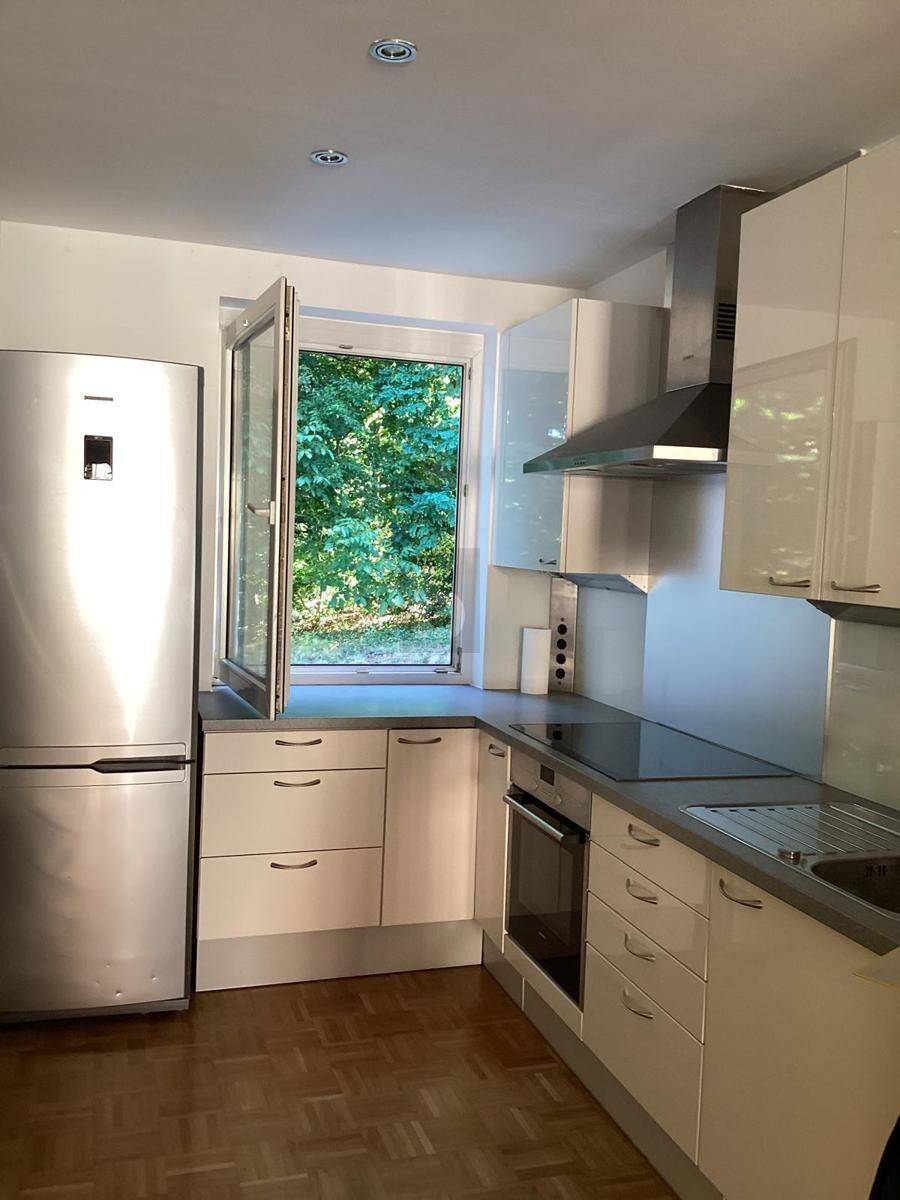 Moderne Einbauküche mit weißen Hochglanzfronten, integrierten Geräten und Fenster mit Grünblick.