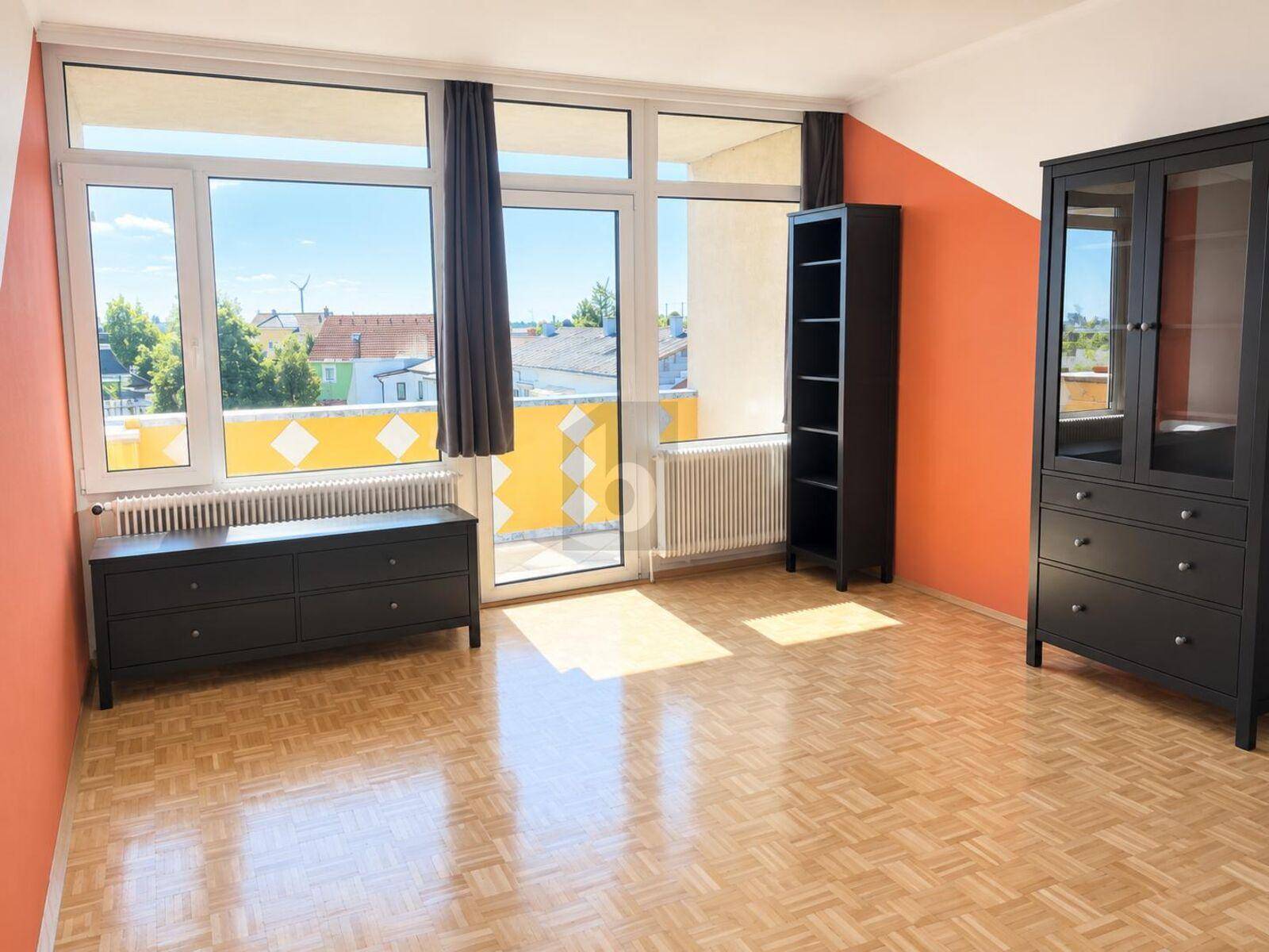 Heller Wohnraum mit Parkettboden, Zugang zum Balkon und Blick ins Grüne.