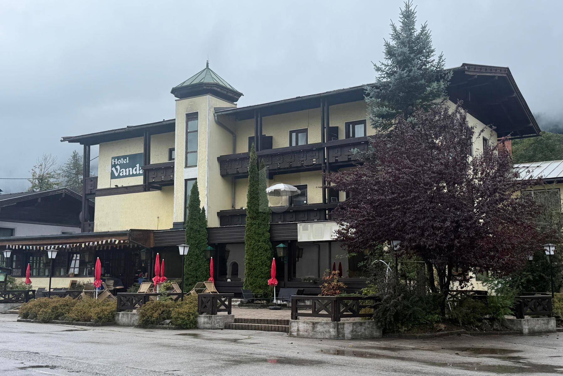 Außenansicht eines Hotels mit traditioneller Architektur, Balkonen und einem kleinen Turm unter bewölktem Himmel.