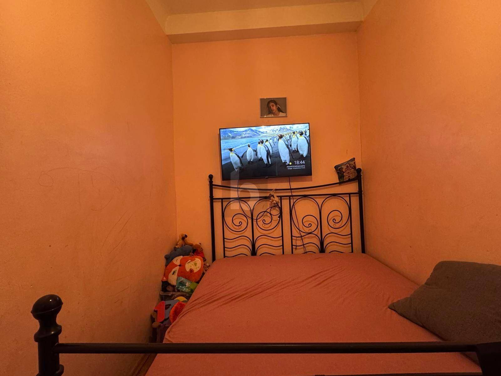 Ein gemütliches Schlafzimmer mit orangefarbenen Wänden, einem schmiedeeisernen Bett und einem an der Wand montierten Fernseher.
