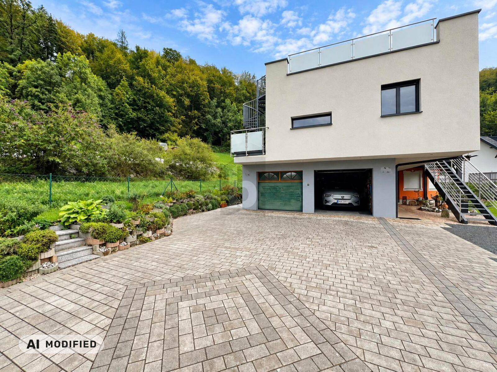 Ansicht des modernen Hauses mit integrierter Garage, gepflasterter Zufahrt und grüner Umgebung.