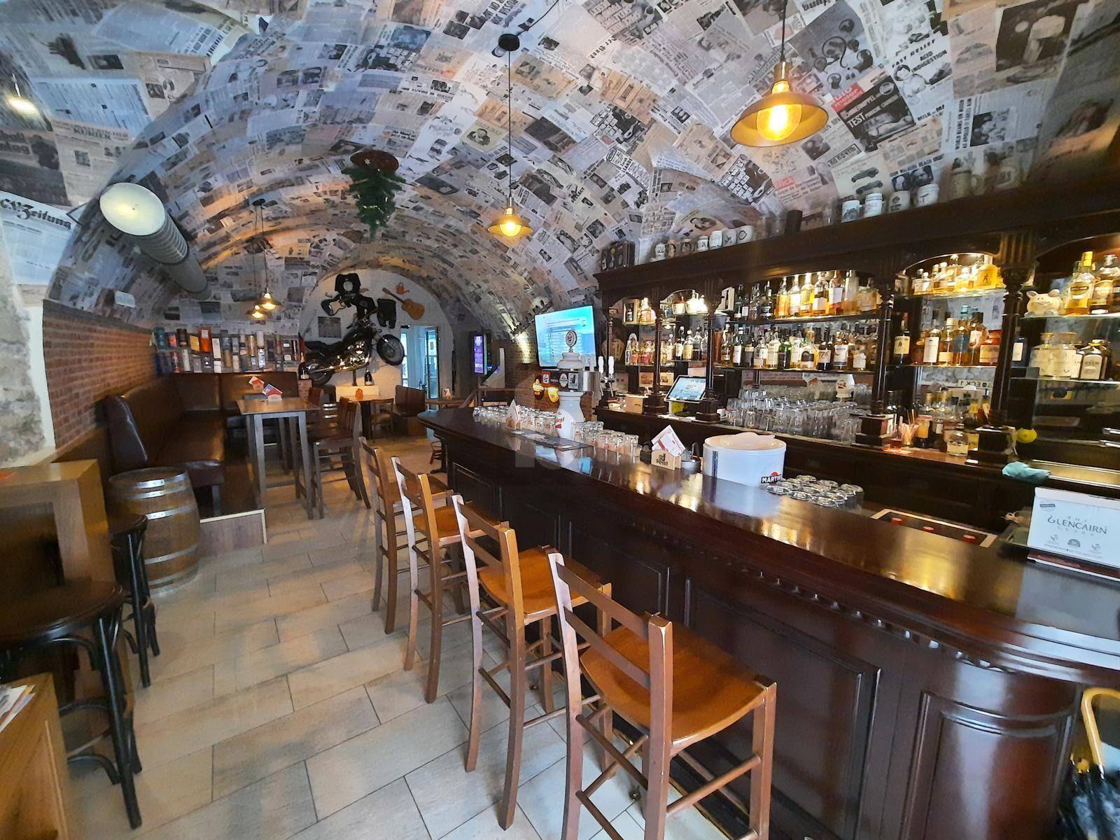 Gewölbter Innenraum einer Bar mit Zeitungsartikeln an der Decke und einer langen Holztheke.