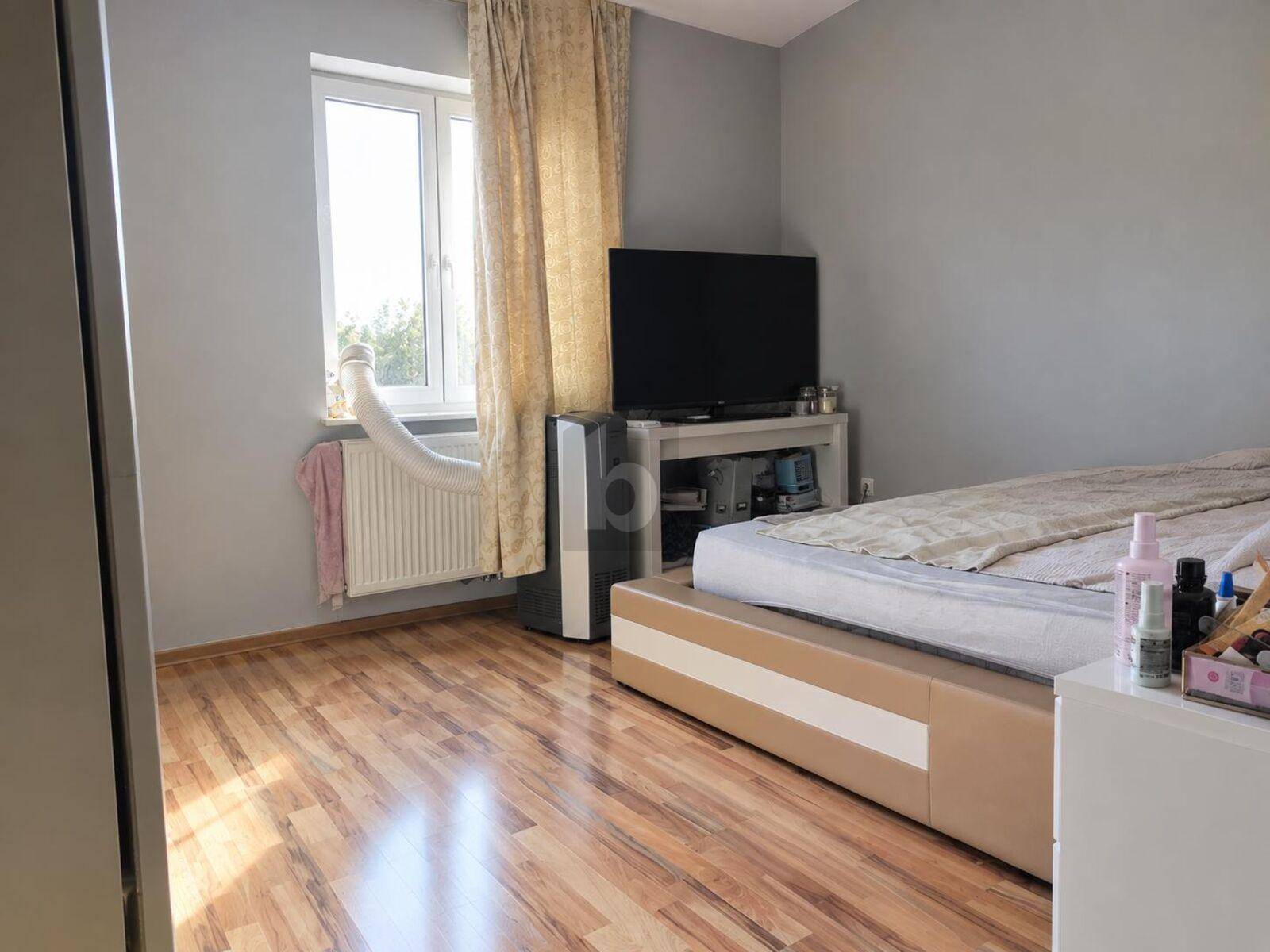Schlafzimmer mit Holzboden, großem Fenster und mobiler Klimaanlage für angenehme Temperaturen.
