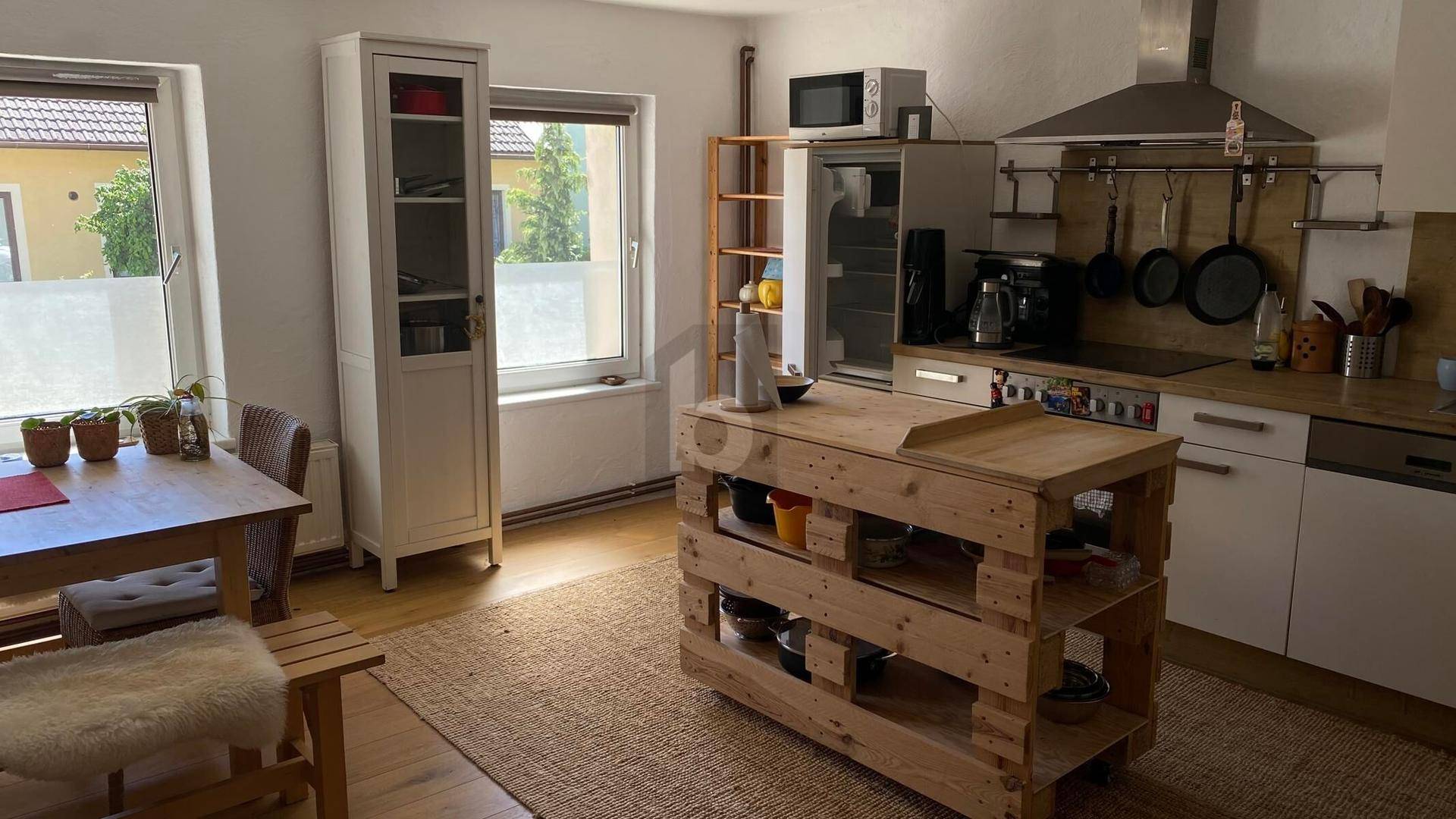 Helle Wohnküche mit Holztisch, Kücheninsel aus Paletten und modernen Geräten.