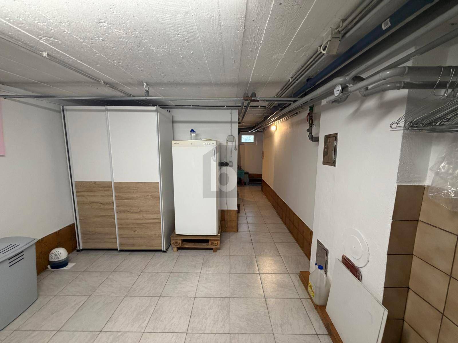 Geräumiger Kellerraum mit Fliesenboden, Lagerregalen und sichtbaren Installationen an der Decke.