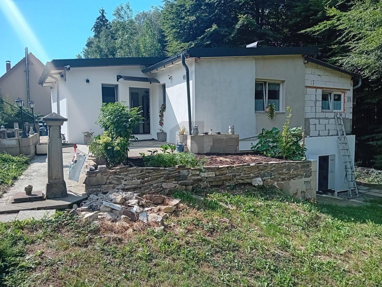 Rückansicht eines weißen Hauses mit Gartenbereich und sichtbaren Bauarbeiten an der Fassade.