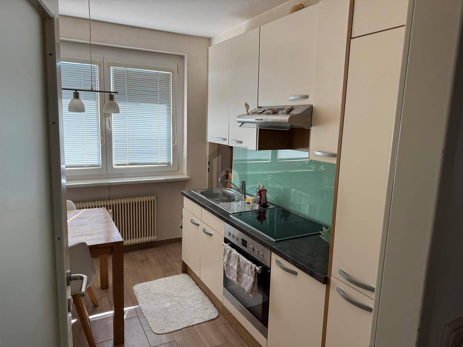 Funktionale Küche mit hellen Schränken, Kochfeld und Fenster mit Blick nach draußen.