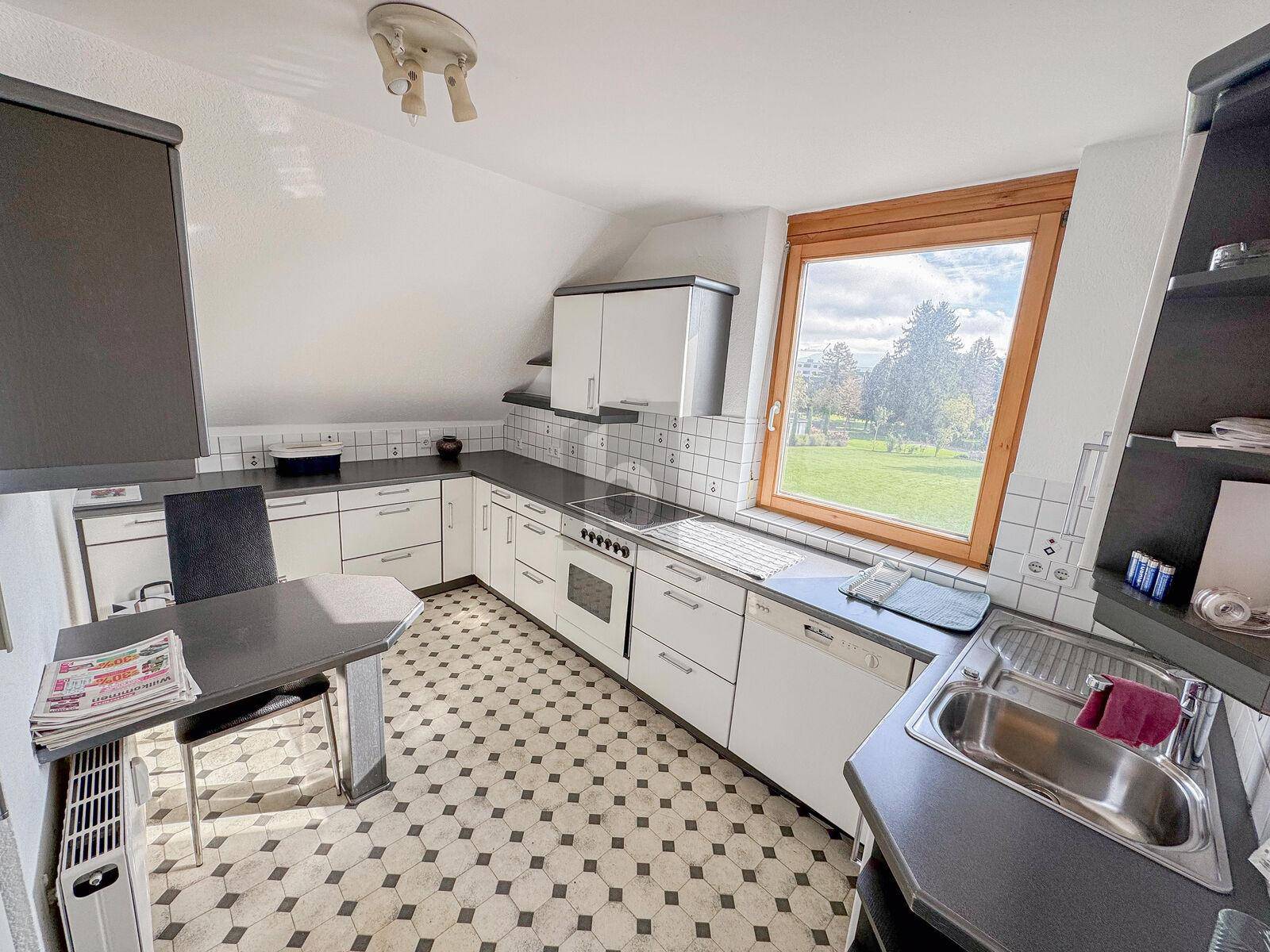 Funktionale Küche mit Dachschräge, schwarz-weißem Fliesenboden und Fenster mit Blick ins Grüne.
