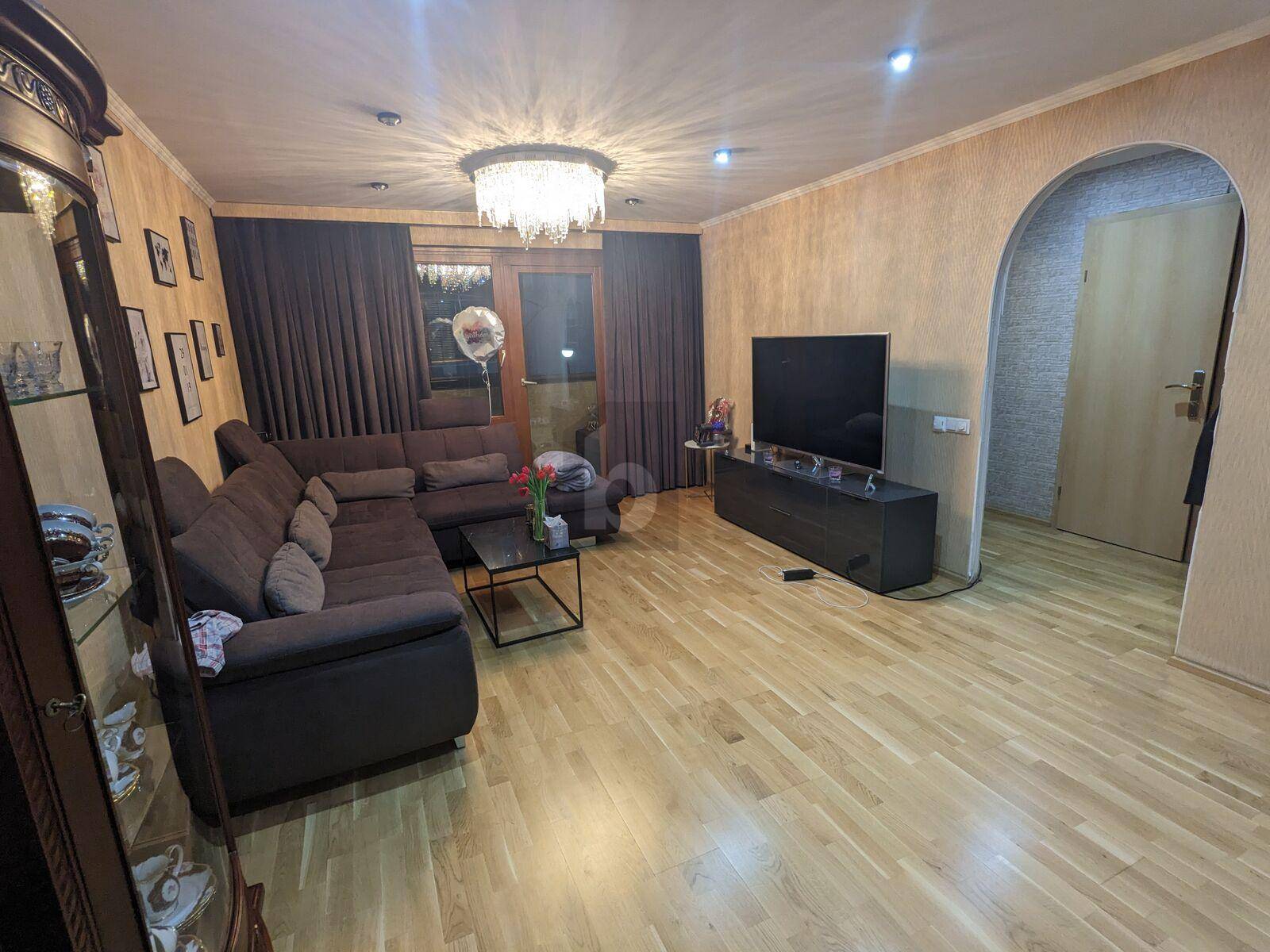 Gemütliches Wohnzimmer mit großem Ecksofa, Holzboden und Zugang zu einem weiteren Bereich durch einen Bogen.
