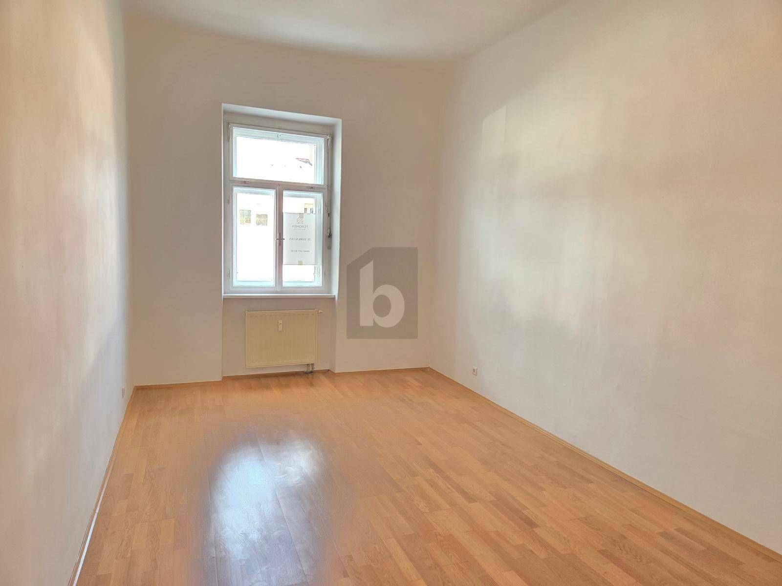 Leerer Raum mit hellem Laminatboden und großem Fenster für viel Tageslicht.