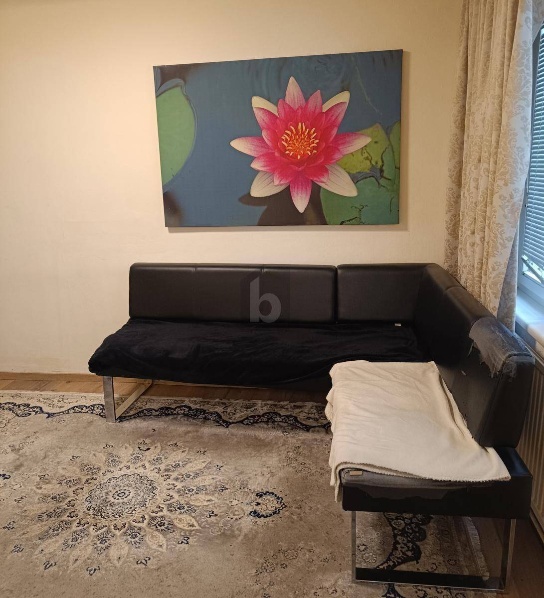 Gemütliche Ecke mit schwarzem Ledersofa, Teppich und großem Wandbild einer Seerose.