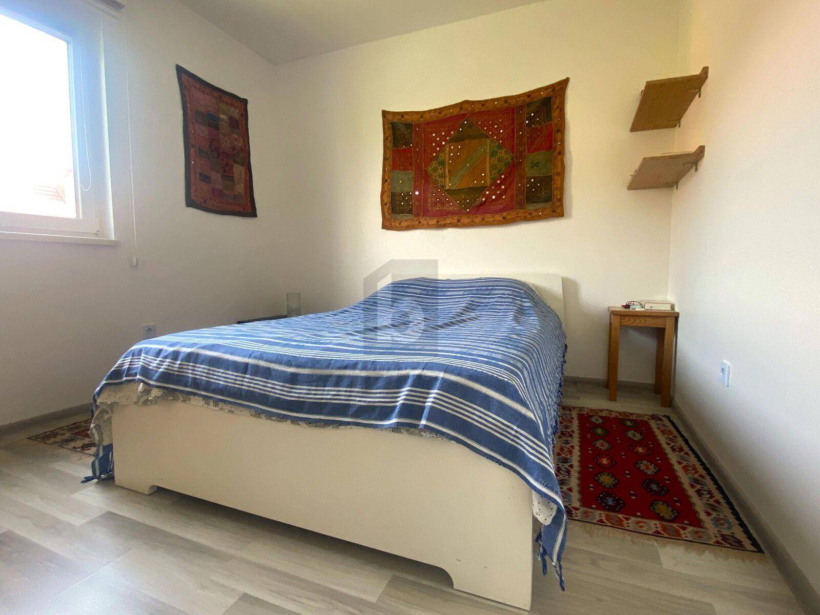 Gemütliches Schlafzimmer mit Bett, Holzboden und farbigen Teppichen, hell und einladend.