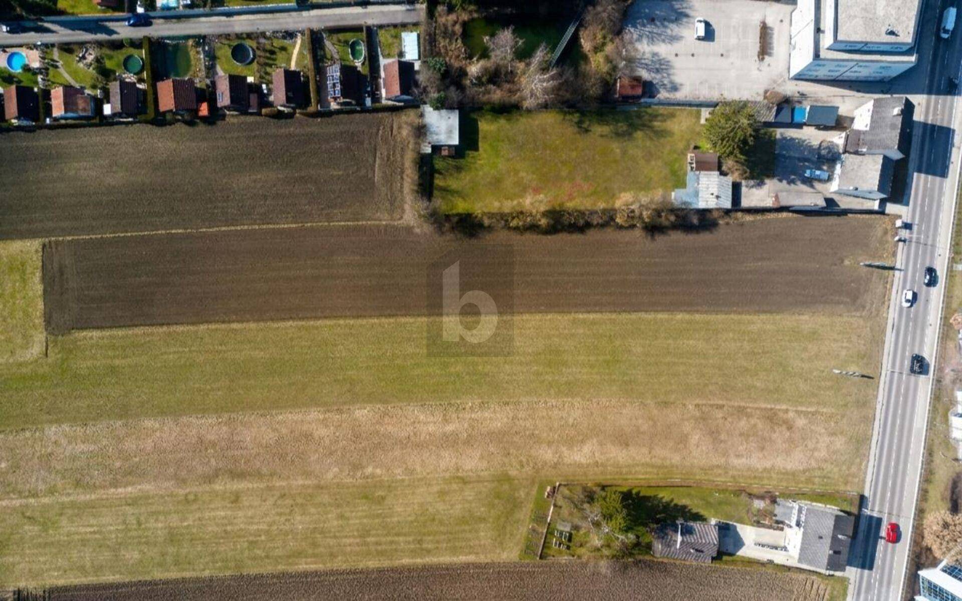 Senkrechte Luftaufnahme von Ackerland, einer Straße und kleinen Gebäuden am Rand.