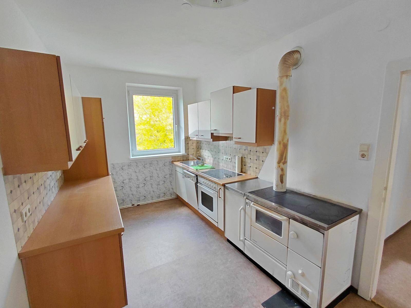 Einfache Küche mit traditionellem Holzofen, weißen Schränken und Fenster.