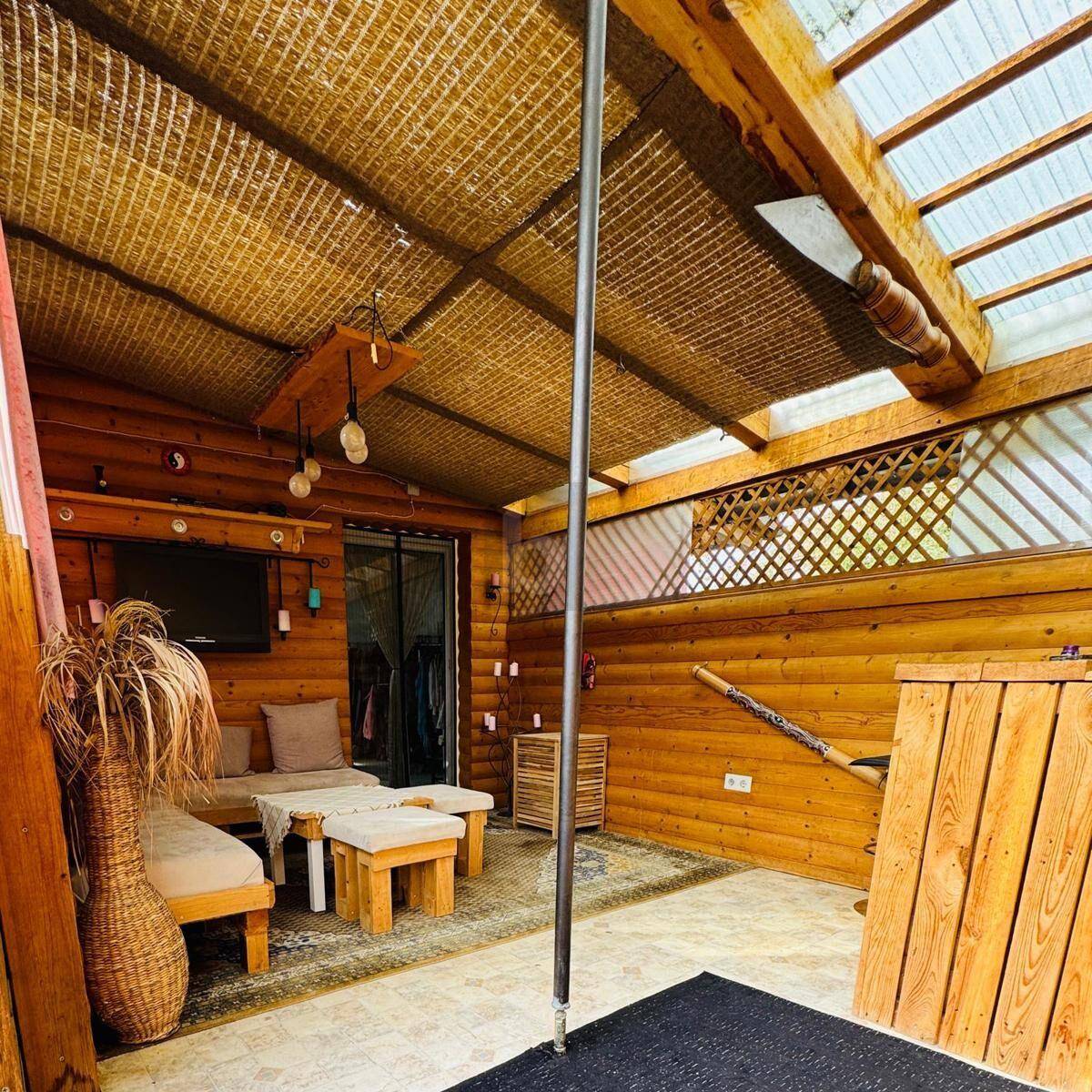 Gemütlicher Wintergarten mit Holzwänden, Rattanmöbeln und viel Tageslicht.