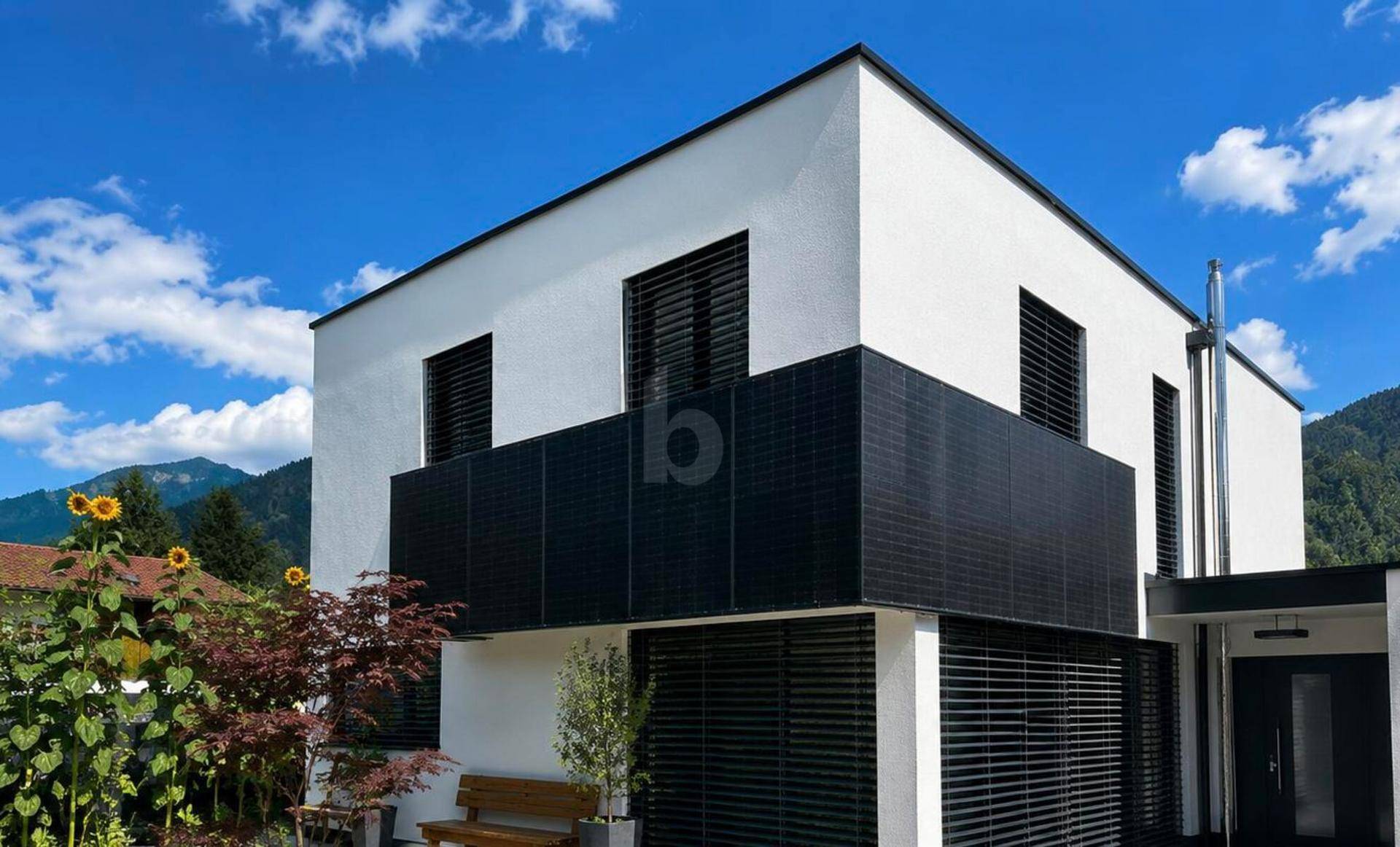 Moderne Architektur mit weißer Fassade, schwarzen Akzenten und Blick auf die Berge.