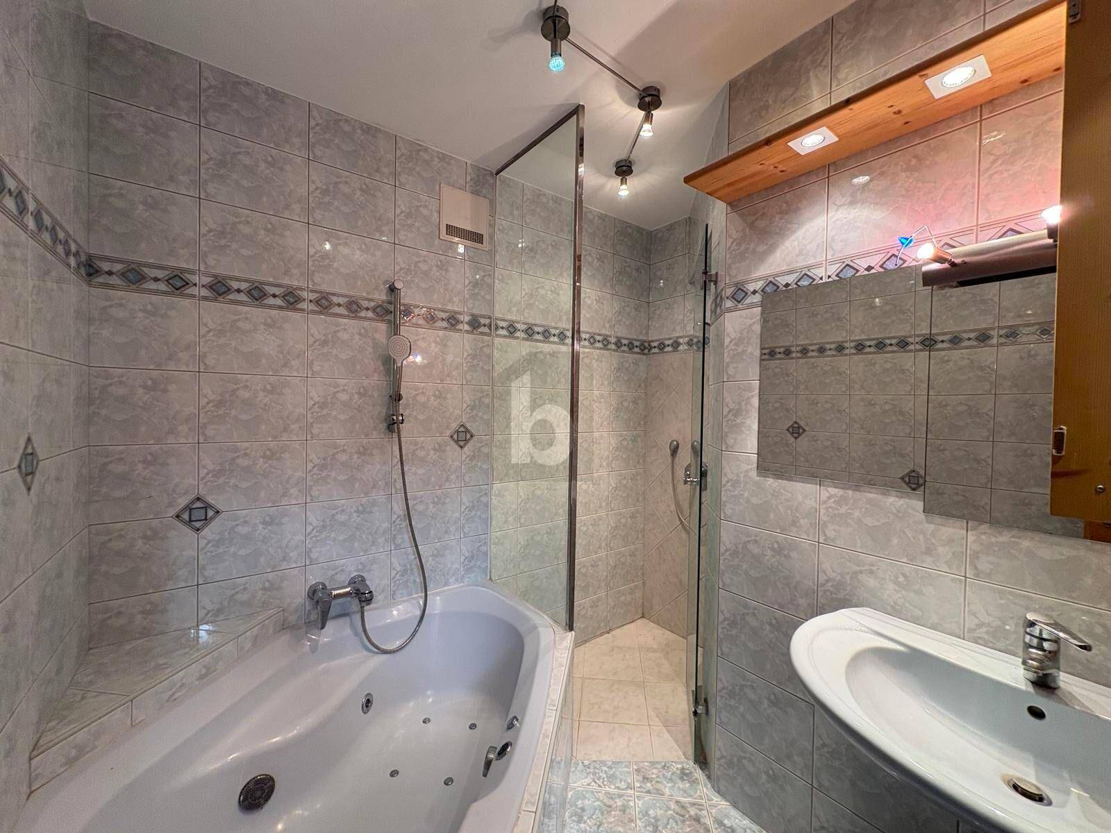 Gefliestes Badezimmer im Stil der 80er Jahre mit Badewanne, separater Dusche und einem Waschbecken.