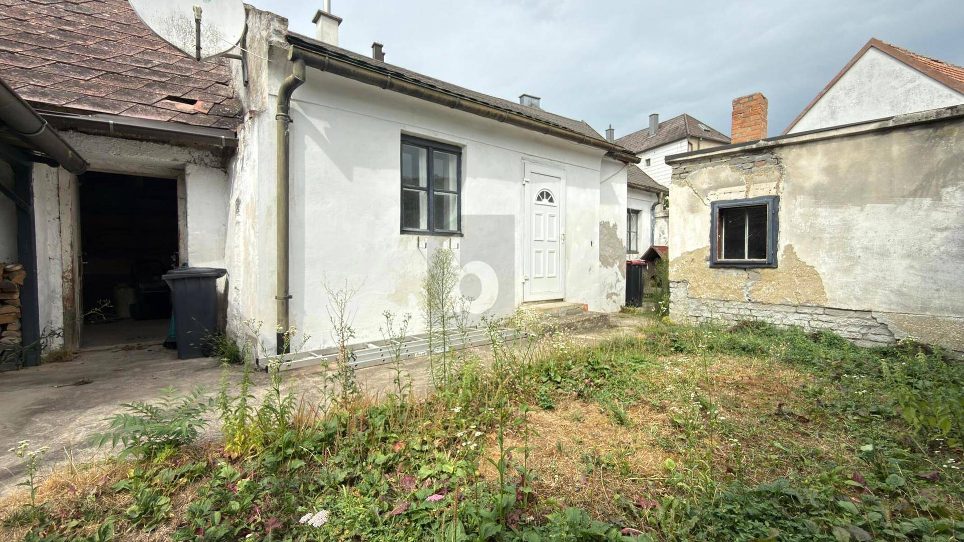Hinterhof mit ungepflegtem Gartenbereich und der Rückseite eines Wohnhauses.