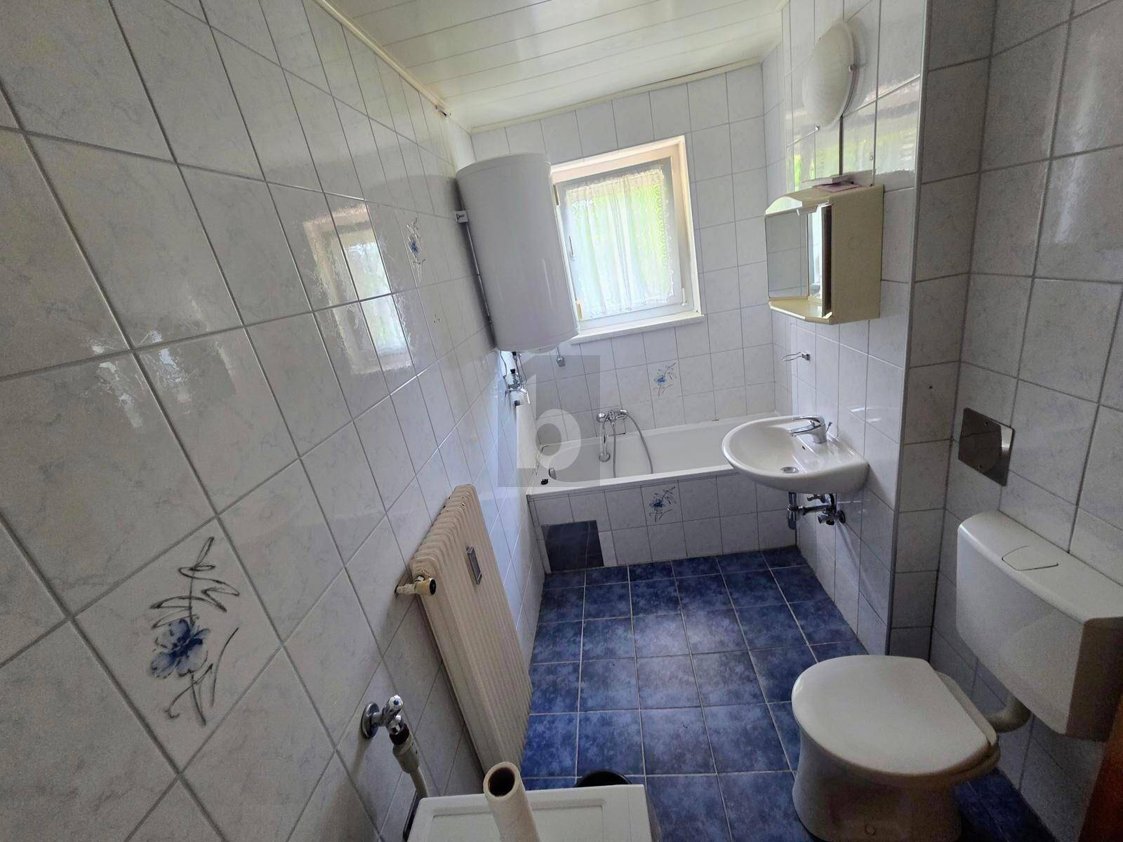 Badezimmer mit blauen und weißen Fliesen, Badewanne, WC und Fenster.