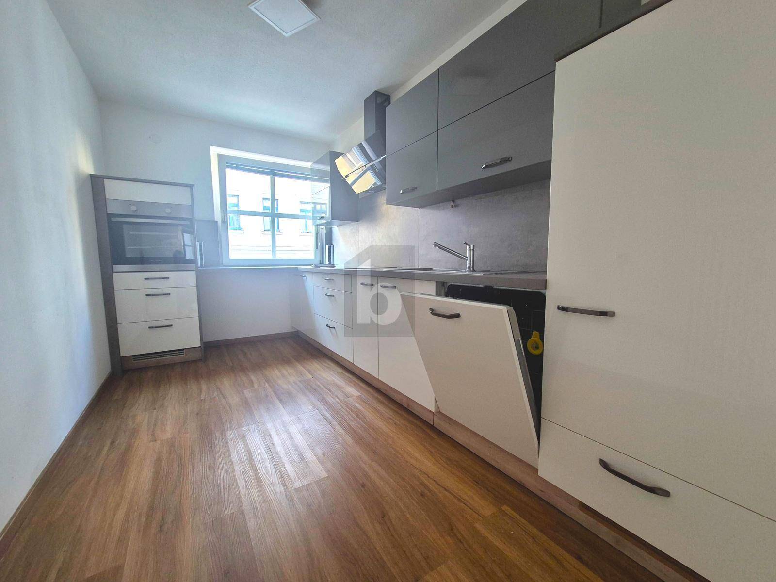 Moderne Küche mit grauen und weißen Schränken, Einbaugeräten und Laminatboden.