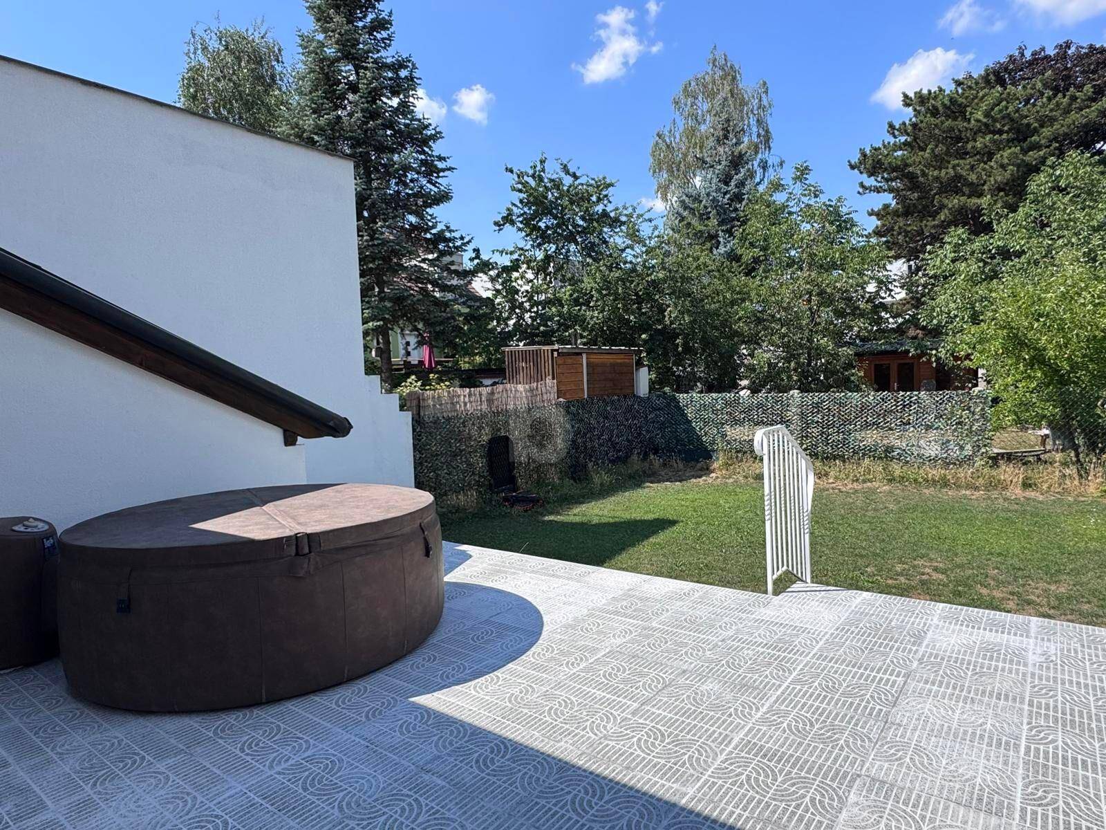 Sonniger Außenbereich mit gepflasterter Terrasse, einem Whirlpool und Blick ins Grüne.
