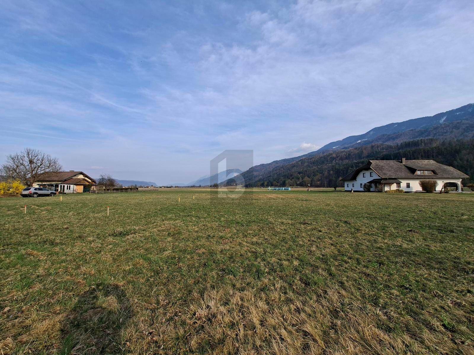 Offenes Feld mit weitem Blick auf die umliegende Berglandschaft und einige Gebäude.