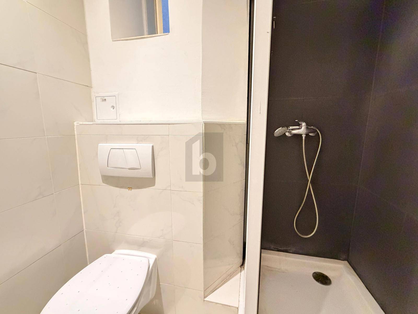 Kleines Badezimmer mit Toilette und Duschbereich, gefliest in Weiß und Dunkelgrau.