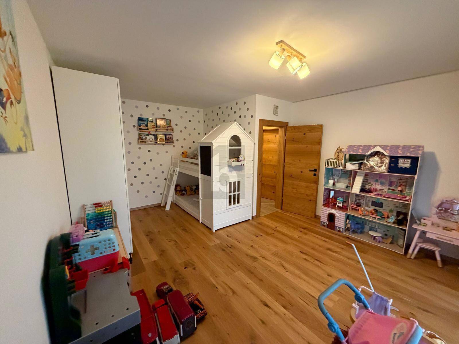 Kinderzimmer mit Etagenbett in Hausform, Holzboden und Spielzeug für Kinder.