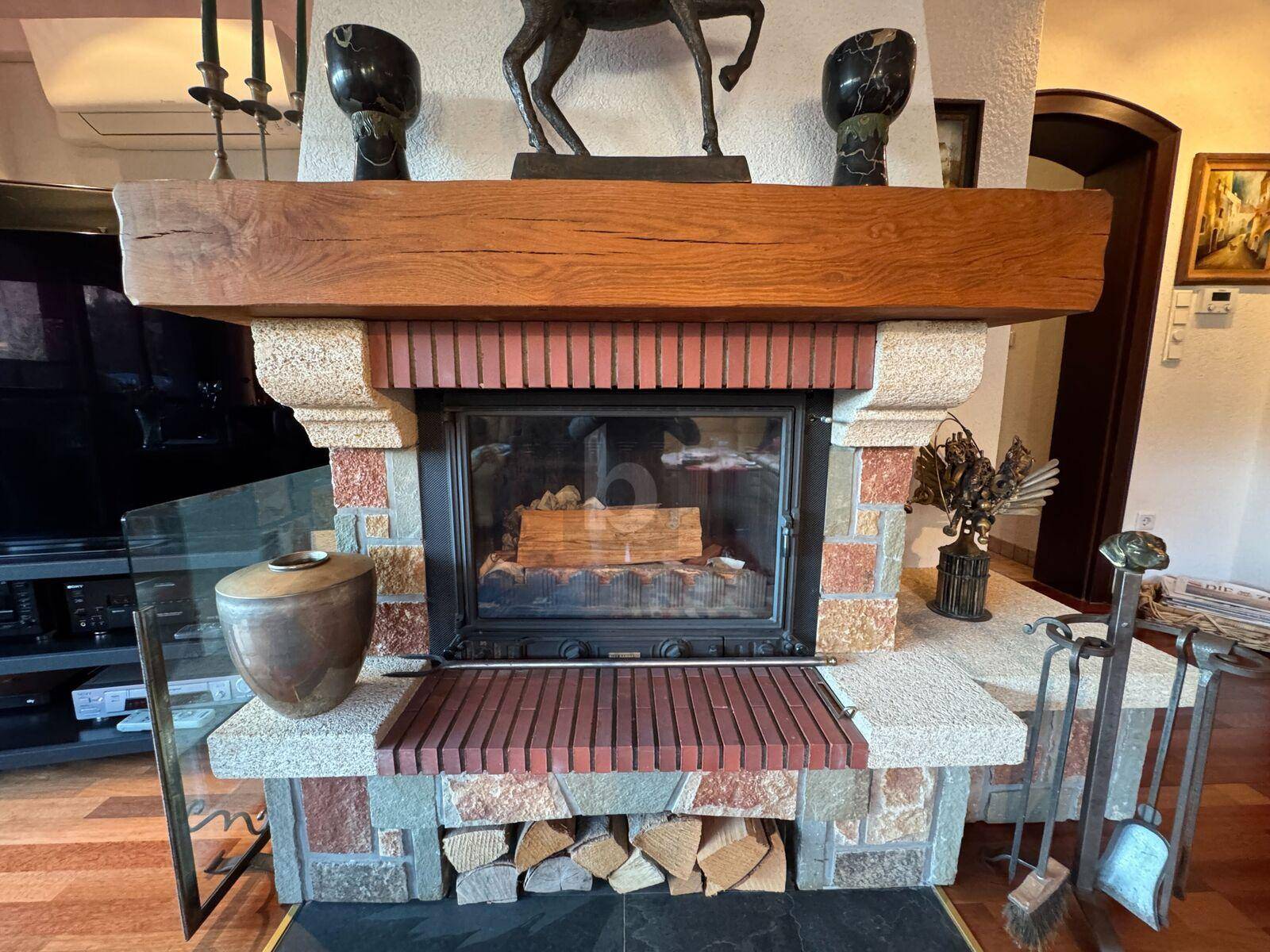 Gemütlicher Kamin mit Holzscheiten und rustikalem Holzbalken als Sims.
