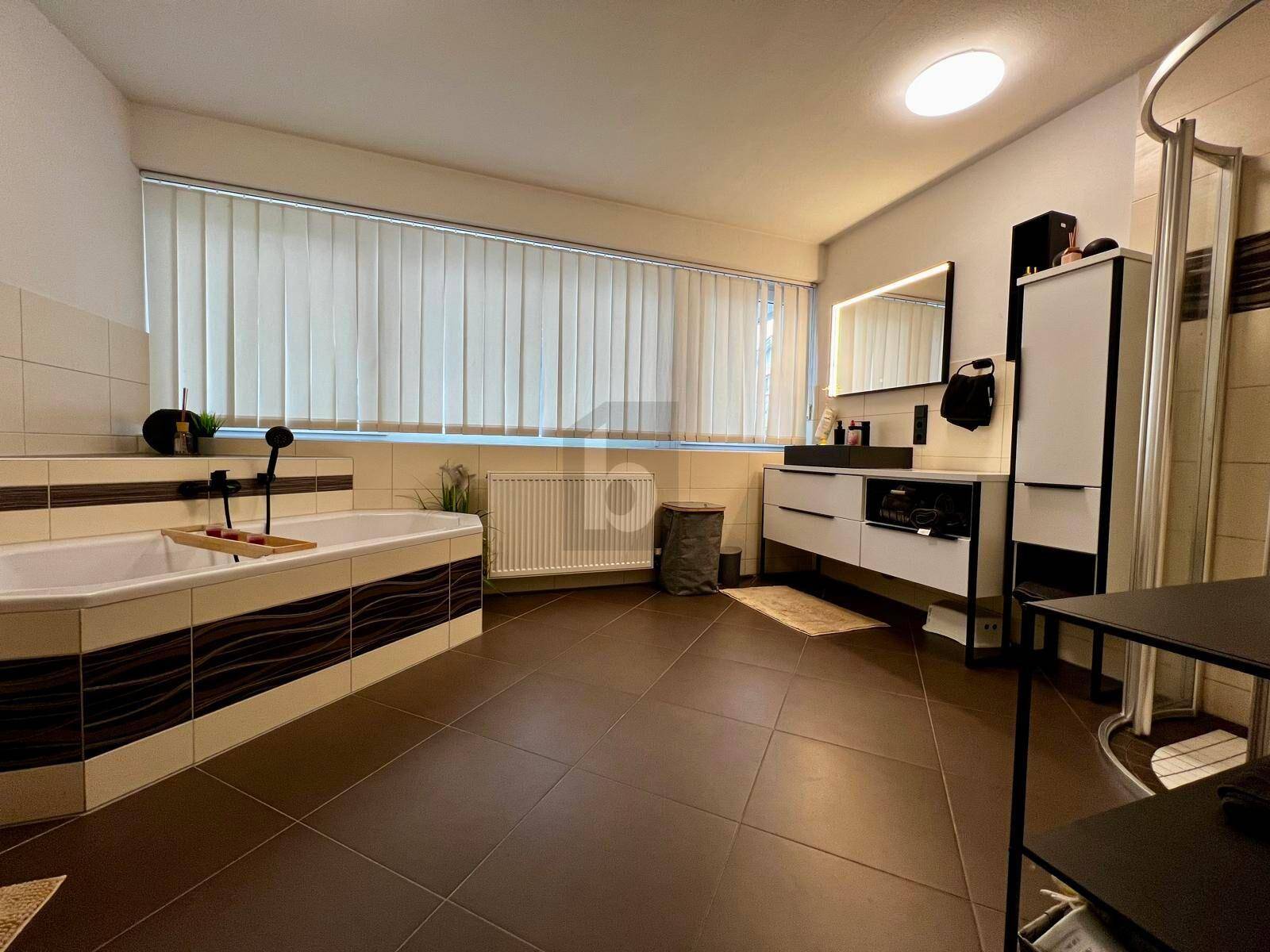 Geräumiges Badezimmer mit Badewanne, Duschkabine, Doppelwaschbecken und großem Fenster.