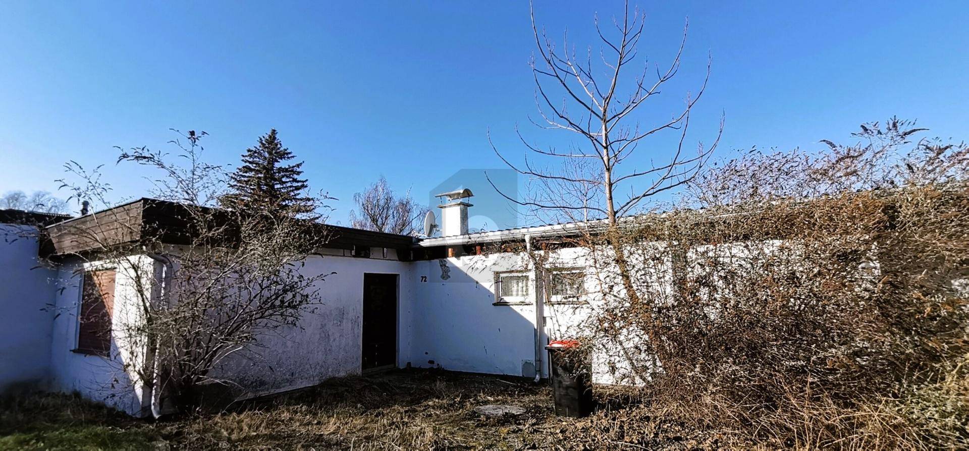 Seitenansicht eines weißen Einfamilienhauses mit dunklem Dach und kahlen Bäumen im Winter.