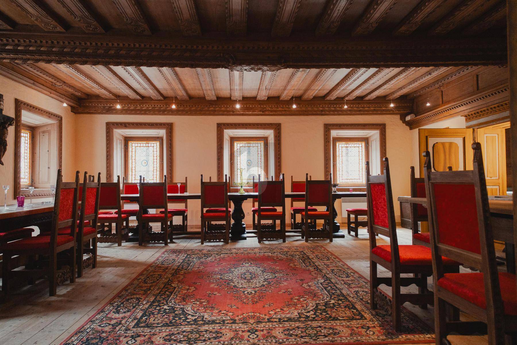 Großer traditioneller Speisesaal mit Holzbalkendecke, Holzboden und roten Stühlen.
