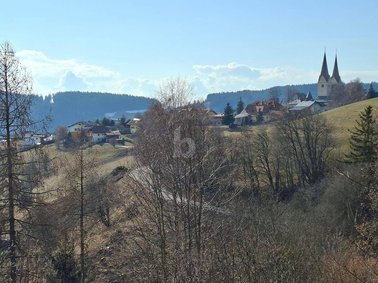 Panoramablick auf eine malerische Dorflandschaft mit Kirchtürmen und bewaldeten Hügeln.