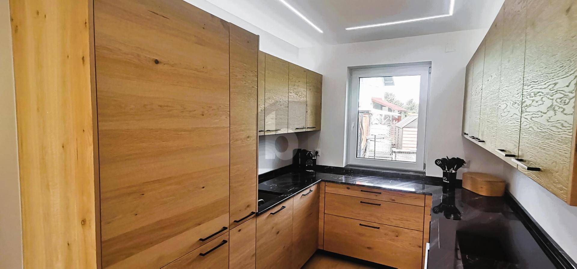 Moderne Küche mit Holzfronten, dunklen Arbeitsplatten und einem Fenster für natürliches Licht.