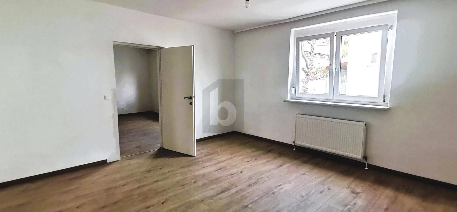 Heller, leerer Raum mit Laminatboden, Fenster und Heizkörper, bereit zur Einrichtung.