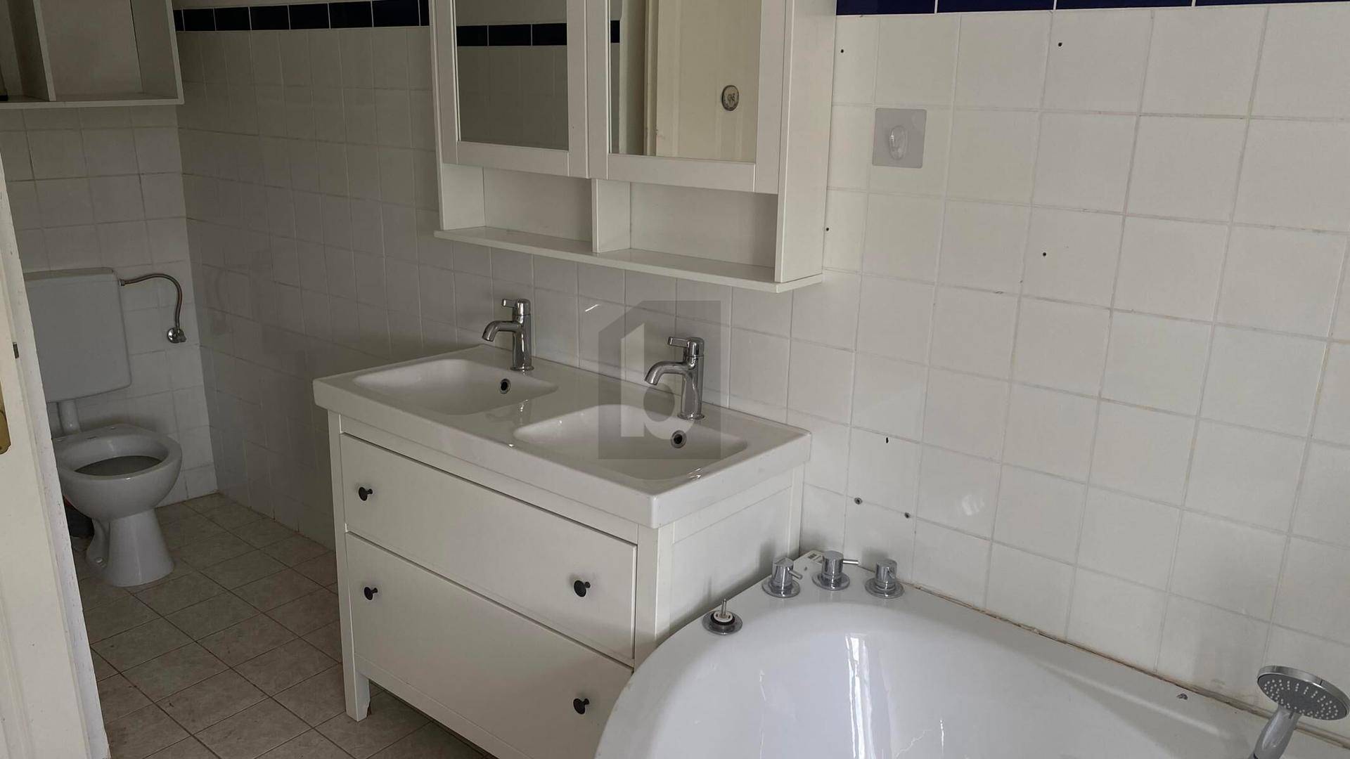 Helles Badezimmer mit Doppelwaschbecken, Badewanne und weißen Fliesen.