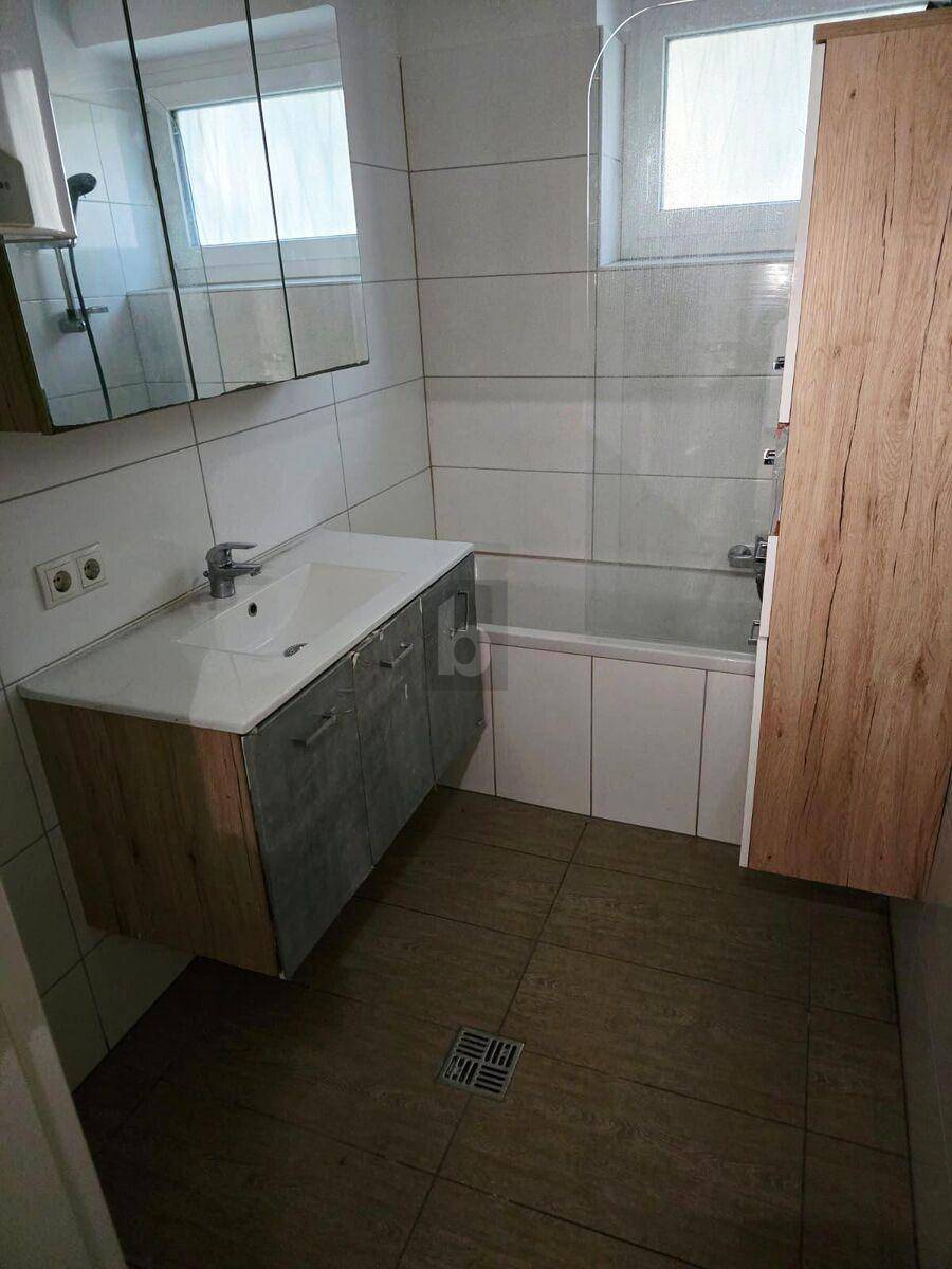 Badezimmer mit Badewanne, Waschbecken, Spiegelschrank und hellen Fliesen.
