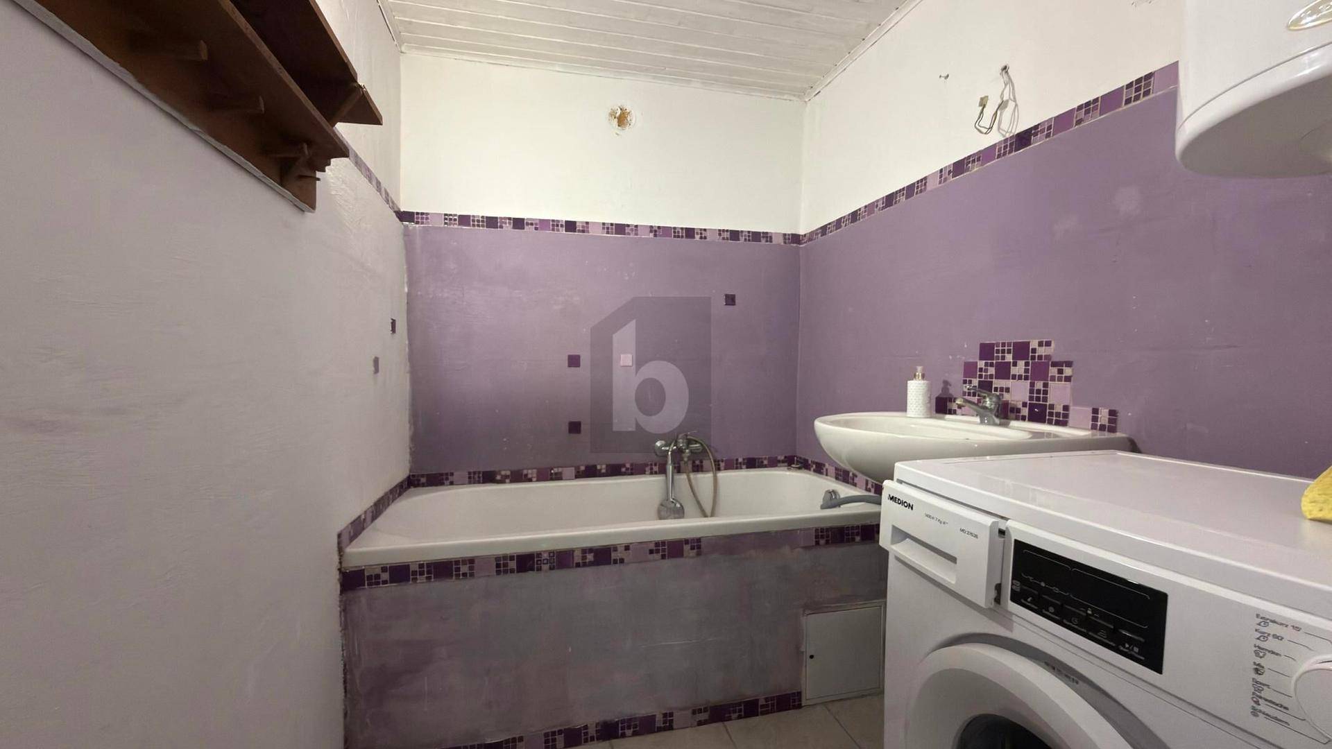 Badezimmer mit Badewanne, Waschbecken und Waschmaschine, ausgestattet mit lila Fliesen.