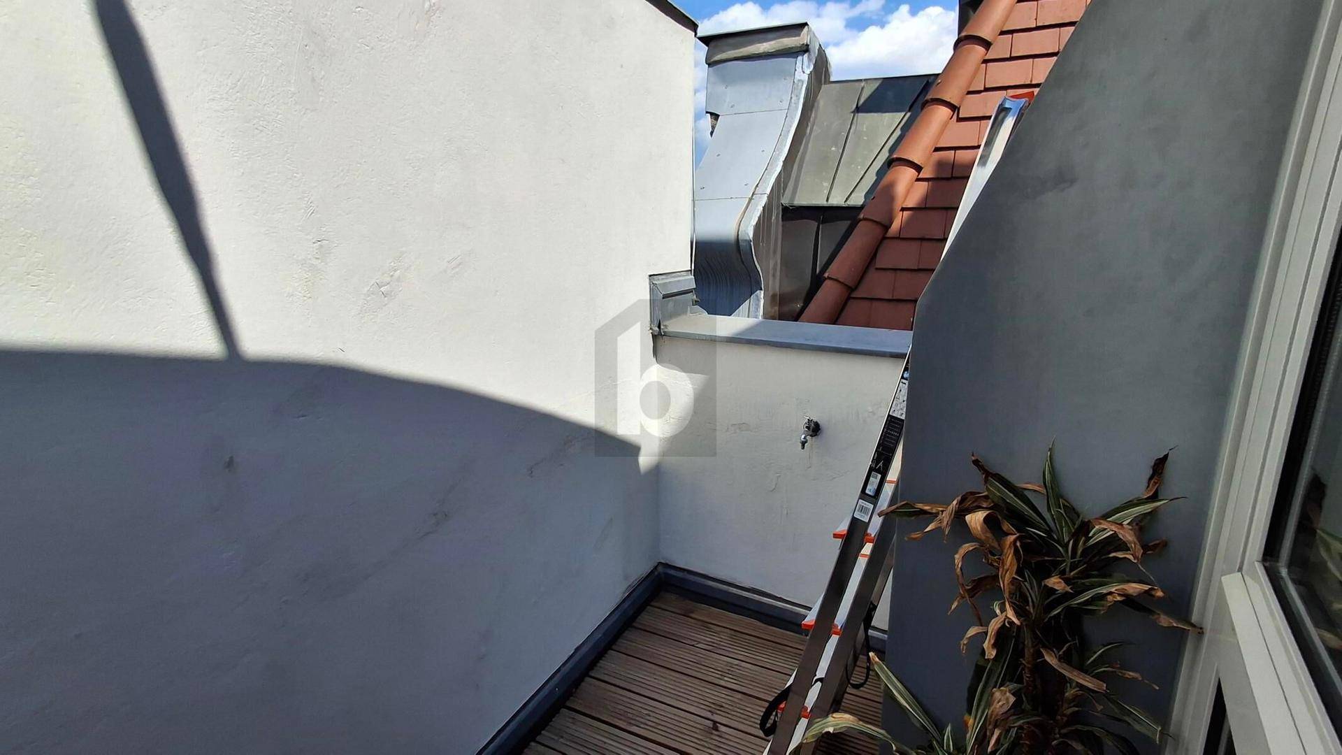 Kleiner Balkon mit Holzboden und Blick auf die umliegenden Dächer.