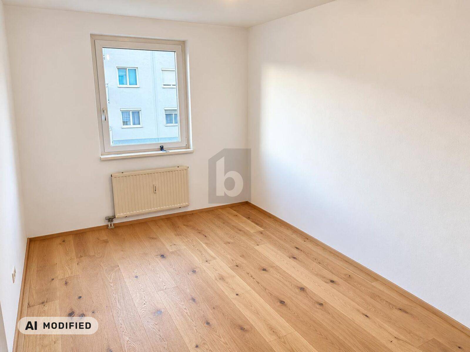 Helles Zimmer mit Holzparkettboden und Fenster mit Blick auf ein gegenüberliegendes Gebäude.
